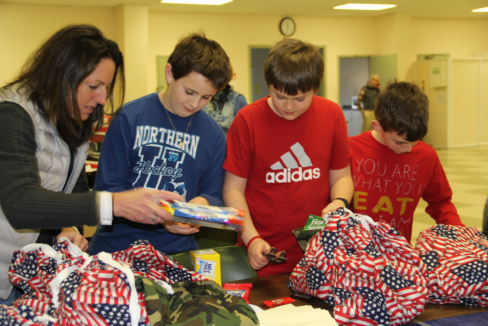 Southold Elementary teacher Patty Mellas helps students Ben Ward, Aidan Russell, both 11, and Tate Klipstein, 10, pack care packages for veterans. (Credit: Carrie Miller)